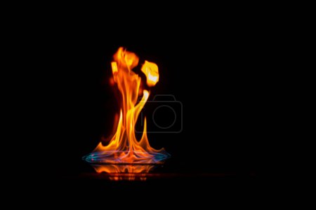 Foto de Llama intensa, fuego, ardiendo brillantemente sobre un fondo oscuro, sobre una superficie de espejo con reflejo, peligro, catastrófico - Imagen libre de derechos