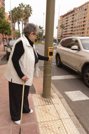 An elderly man uses a pedestrian crossing button on a city street. Smart city, comfort and safety technologies
