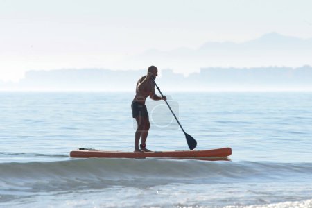 Silueta de un kayak en un kayak de remo personal, remando un kayak con un remo en las tranquilas aguas del océano al amanecer sobre el fondo de siluetas de edificios de la ciudad