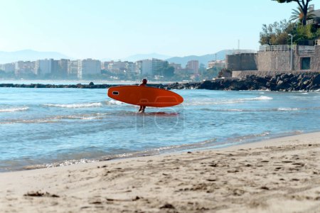 Man Kajaker trägt ein Surfbrett, ein Kajak auf einer Achterbahn vor der Kulisse der Stadt und einen tropischen Blick bei Sonnenaufgang im Hintergrund. Sommersporturlaub auf dem Wasser