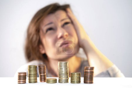 Woman looks up thoughtfully and tensely in front of stacks of coins. Search for a way out of poverty, strategy for solving the economic problem, financial crisis. Calculation, distribution of earnings