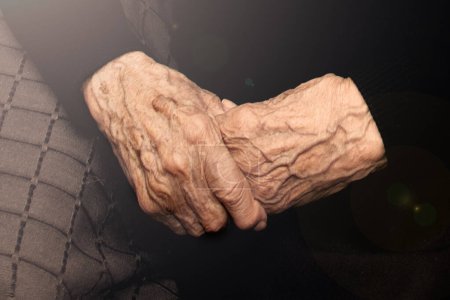 Closeup of the philosophical view of the crossed elderly hands of a centenarian grandmother with protruding veins, wrinkles, age spots conveying wisdom, difficulty, respect for a long life. long-liver