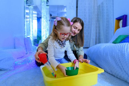 Photo for Child with physical disability in sensory stimulating room, snoezelen. Child living with cerebral palsy interacting with her therapist during therapy session. - Royalty Free Image