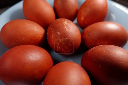 Boiled red-brown Easter eggs in blue plate on table, textured eggshells vivid color contrast