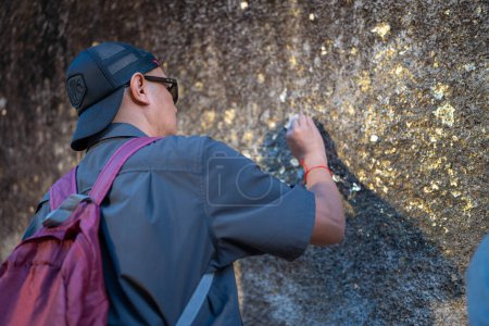 Male tourists pay their respects by covering the giant rocks with gold leaf at Khao Khitchakut National Park, Chanthaburi, Thailand.