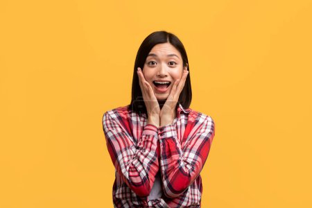 Photo for Unbelievable. Shocked asian lady with open mouth and hands on cheeks, emotionally reacting to news, standing over yellow studio background. Wow offer concept - Royalty Free Image