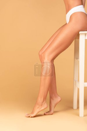 Photo for Cropped of fit caucasian lady showing her smooth legs, hair removing cosmetics, epilation, laser hair removal, waxing concept, beige studio background, copy space - Royalty Free Image