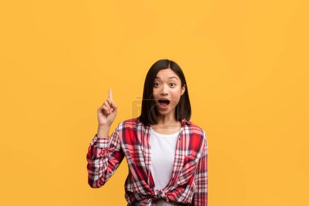 Photo for Great idea, inspiration concept. Emotional asian lady having wow creative idea, raising finger up and looking at camera with open mouth, standing over yellow studio background - Royalty Free Image