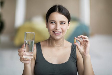 Closeup Portrait Of Smiling Beautiful Female Holding Vitamin Capsule And Glass Of Water At Home, Attractive Happy Woman Recommending Supplements Pill For Health And Beauty, Selective Focus