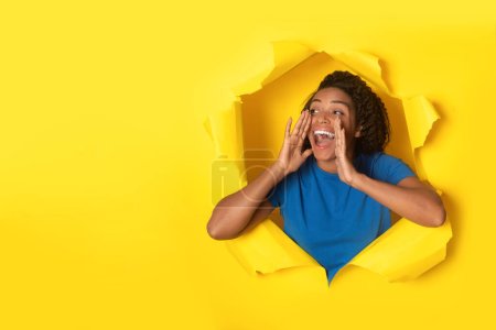 Heureuse femme noire criant tenant les mains près de la bouche publicité Grande offre regardant à côté de l'espace vide posant en papier jaune déchiré arrière-plan. Bannière publicitaire