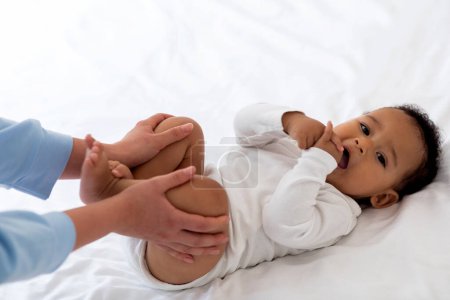 Téléchargez les photos : Constipation chez les bébés. Gros plan d'une mère attentionnée faisant de la gymnastique avec un enfant noir mignon allongé sur le lit, une mère méconnaissable faisant un massage à un petit garçon afro-américain pour soulager les gaz - en image libre de droit