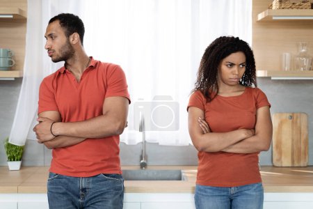 Traurig gekränkter junger schwarzer Mann im roten T-Shirt ignoriert Frau nach Streit, denkt an Trennung in der Küche. Beziehungsprobleme, Stress, Skandal und Emotionen zu Hause während des Covid-19-Ausbruchs