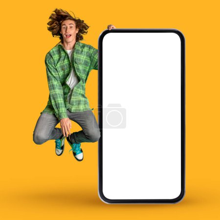 Photo for Amazing Offer. Excited Hipster Guy Jumping Near Big Blank Smartphone Over Yellow Background In Studio, Cheerful Young Male Demonstrating Copy Space For Mobile App Or Website Design, Collage - Royalty Free Image