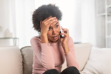 Photo for Sad frightened shocked frustrated millennial african american female, call and talk by smartphone, suffer from stress and bad news in bright living room interior. People emotions, crisis and problems - Royalty Free Image