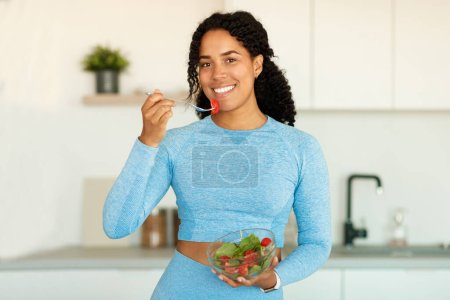 Foto de Concepto de alimentación saludable. Mujer negra feliz en ropa deportiva disfrutando de ensalada de verduras, cenar en la cocina en casa, espacio libre. Nutrición para adelgazar, pérdida de peso recetas de alimentos - Imagen libre de derechos