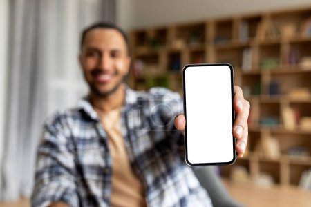 Photo for Excited arab guy showing smartphone with blank white screen at camera, recommending new mobile app or website, sitting at home, selective focus, mockup - Royalty Free Image