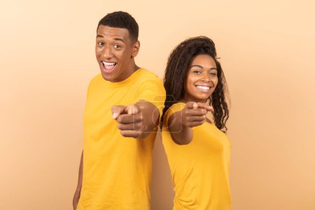 Und was ist mit Ihnen? Positives afrikanisch-amerikanisches Paar zeigt mit dem Zeigefinger in die Kamera und posiert vor buntem Studiohintergrund. Glücklich schwarz kerl und dame auswählen und angeben