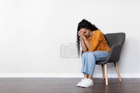 Photo for Upset curly brunette young woman in casual outfit sitting in arm chair, white wall background, crying, millennial lady experiencing midlife crisis, feeling lonely, depressed, panorama, copy space - Royalty Free Image