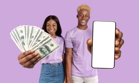 Foto de Alegre afroamericano millennials hombre y mujer apostando en Internet, mostrando un nuevo teléfono inteligente con pantalla blanca vacía y mucho dinero en efectivo, fondo de estudio púrpura, maqueta, collage - Imagen libre de derechos