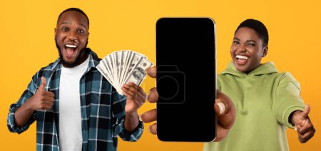 Photo for Cute chubby young black man and woman celebrating success on yellow, showing cash dollars and cell phone with black empty screen, smiling and gesturing thumb ups, trading online, mockup, panorama - Royalty Free Image