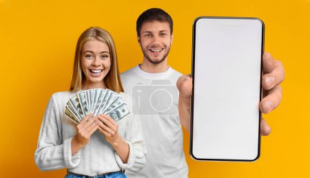 Photo for Cheerful youngsters cute millennial blonde man and woman showing newest smartphone with white blank screen and cash bunch of dollars, mockup, yellow studio background. Online bet concept, collage - Royalty Free Image