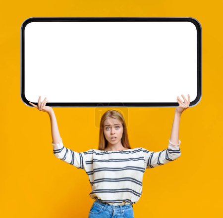 Photo for Confused Young Female Holding Huge Blank Smartphone Above Head, Frustrated Millennial Woman Demonstrating Mobile Phone With White Empty Screen For Mockup, Advertising Online Offer, Collage - Royalty Free Image