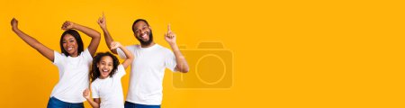 Photo for Cheerful african american family enjoying time together on yellow studio background, happy black father, mother and daughter in white t-shirts dancing and smiling, panorama with copy space, collage - Royalty Free Image