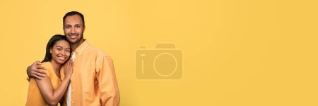 Téléchargez les photos : Beau couple afro-américain heureux embrassant et souriant à la caméra, large bannière horizontale pour l'offre familiale avec jeunes conjoints noirs posant sur fond jaune studio, Panorama avec espace de copie - en image libre de droit