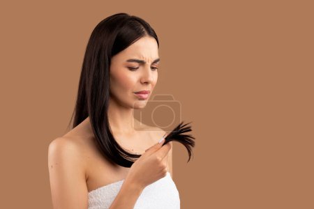 Photo for Unhappy half-naked brunette young woman holding her long hair split ends in hand, isolated on beige background, need for haircare mask treatment, diet correction, balm, vitamins, copy space for advert - Royalty Free Image