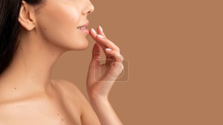 Photo for Concept of using lipbalm in cold weather. Unrecognizable topless woman using moisturizing balm for lips, isolated on beige studio background, panorama with copy space, closeup shot, side view, cropped - Royalty Free Image