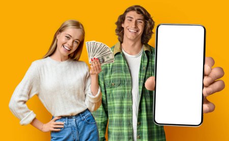 Photo for Cheerful hipsters young man and woman celebrating success on yellow, couple gambling online, showing cell phone with white blank screen and bunch of dollars, yellow background, mockup, studio shot - Royalty Free Image
