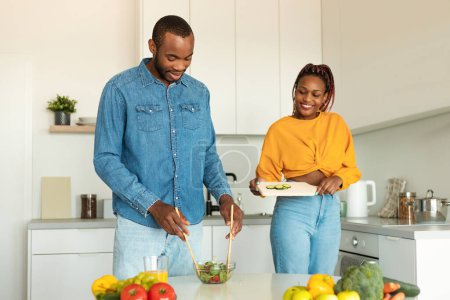 Téléchargez les photos : Joyeux jeunes conjoints noirs cuisine salade de légumes frais ensemble dans la cuisine, profiter de la préparation des aliments sains et passer du temps à la maison, copier l'espace - en image libre de droit