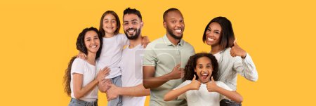 Téléchargez les photos : Joyeux Moyen-Orient et les familles afro-américaines maris et femmes avec des enfants posant sur fond de studio jaune, embrassant, souriant, montrant pouces levés, panorama avec espace de copie. Concept de famille - en image libre de droit