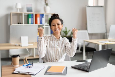 Business luck. Overjoyed female entrepreneur using laptop and shaking fists in joy, celebrating great news, sitting at workplace in office. Successful entrepreneurship career concept