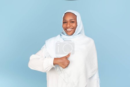 Téléchargez les photos : Comme ça. Heureuse femme afro-américaine en hijab montrant pouce vers le haut à la caméra, souriante dame musulmane recommandant une grande offre, signe gestuel d'approbation, debout sur fond de studio bleu - en image libre de droit