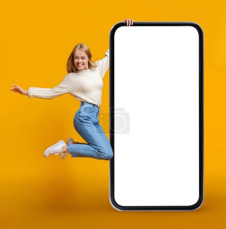Photo for Overjoyed Young Woman Jumping With Huge Blank Smartphone Over Yellow Background, Happy Cheerful Female Demonstrating Copy Space For Mobile Offer Or Advertisement Design, Collage, Mockup - Royalty Free Image