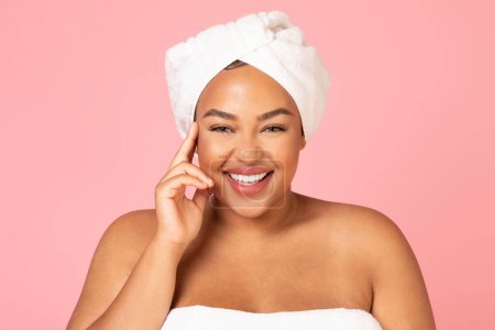 Téléchargez les photos : Belle femme africaine américaine oversize avec serviette blanche sur la tête, appréciant sa jeune beauté et souriant à la caméra, debout sur fond de studio rose, bannière - en image libre de droit