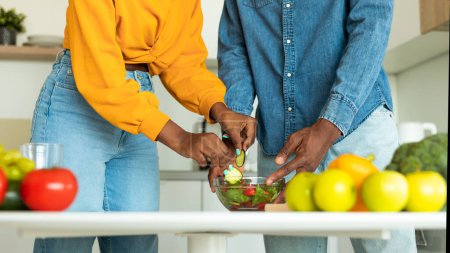 Téléchargez les photos : Cropped image of african american spouses cooking healthy vegetarian food in kitchen, couple noir préparant une salade de légumes pour le déjeuner, panorama, gros plan - en image libre de droit