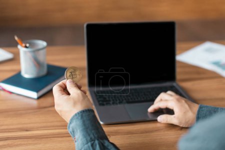 Photo for Mature man work on computer with empty screen hold bitcoin coin at table in office home interior, cropped. Gadget and app for modern business remotely, finance planning, cryptocurrency and investments - Royalty Free Image