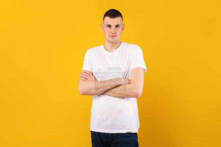 Photo for Male portrait. Handsome caucasian guy with folded arms looking at camera, wearing white t-shirt, posing isolated over yellow studio background. Positive casual male model - Royalty Free Image