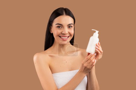 Photo for Close up beauty portrait of cheerful beautiful brunette half-naked woman showing bottle with face care product, recommending nice lotion or milk, isolated over beige studio background, copy space - Royalty Free Image