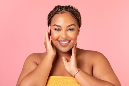 Photo for Beauty care concpet. Portrait of beautiful black chubby woman wrapped in towel touching face with hands, enjoying spa time and skincare treatments result, posing over pink studio background - Royalty Free Image