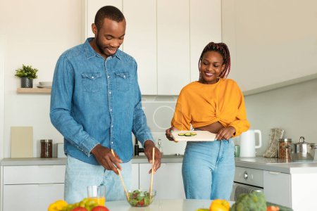 Photo for African american couple cooking together in modern kitchen, enjoying preparing dinner, family making salad at home. Nutrition, cooking, healthy recipes - Royalty Free Image