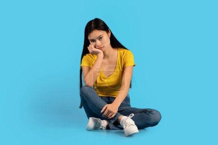 Photo for Sad upset tired millennial korean woman student sitting on floor, suffering from pressure and overwork, isolated on blue background, studio. Problems, stress, depression, bad mood and human emotions - Royalty Free Image