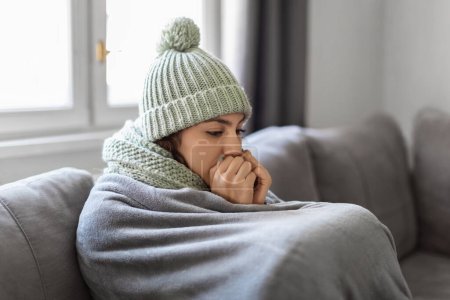 Photo for Heating Problems. Closeup Shot Of Young Woman Freezing At Home, Upset Arab Female Sitting On Couch Covered In Blanket And Warming Her Hands With Breath, Sad Lady Feeling Cold Indoors, Copy Space - Royalty Free Image