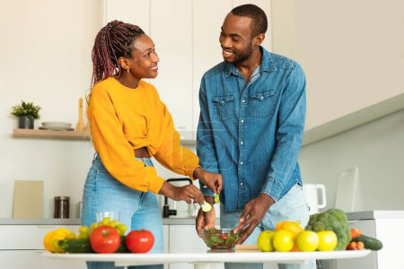 Téléchargez les photos : Aimer les conjoints afro-américains cuisiner ensemble dans la cuisine moderne à la maison, faire une salade saine pour le dîner, regarder et sourire à l'autre. Nutrition et recettes familiales - en image libre de droit