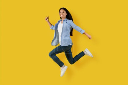 Photo for Glad happy cute millennial korean lady student in casual jumping and freezing in air enjoy freedom, has fun alone, isolated on yellow background, studio. Lifestyle, education, huge sale, ad and offer - Royalty Free Image