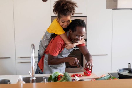 Photo for African American Father And Daughter Having Fun While Cooking Together In Kitchen, Black Dad And Preteen Female Child Preparing Healthy Lunch At Home, Kid Piggybacking Daddy, Copy Space - Royalty Free Image