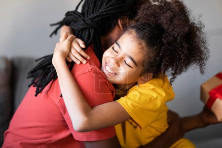 Foto de Concepto del Día del Padre. Happy Preteen Black Girl Abrazando a su papá en casa, Linda hija cariñosa Abrazando al papá afroamericano después de dar un regalo, Saludo con días festivos, Primer plano - Imagen libre de derechos