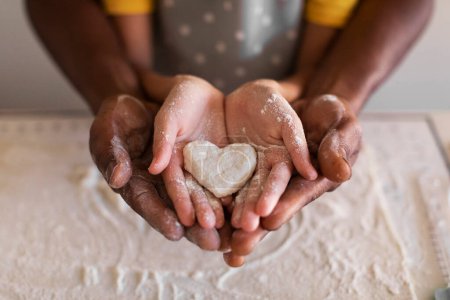 Foto de Primer plano Shot of Black Father and Little Daughter holding Heart Shape made of Dough In Hands, Loving African American Family Dad and Female Child Baking Together In Kitchen, Cropped Shot - Imagen libre de derechos